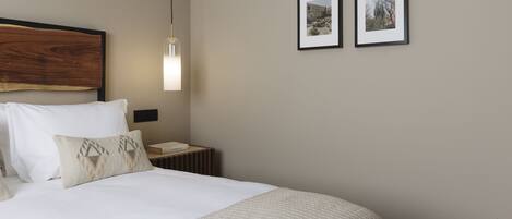 A neatly made bed with a wooden headboard, a bedside lamp, and two framed pictures on the wall.
