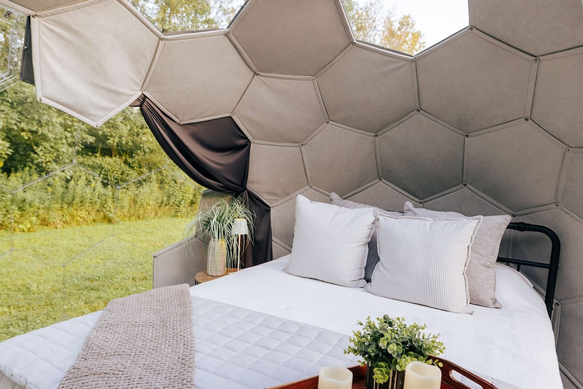 A bed with a hexagonal headboard, a wooden tray with candles, and a view of greenery outside.