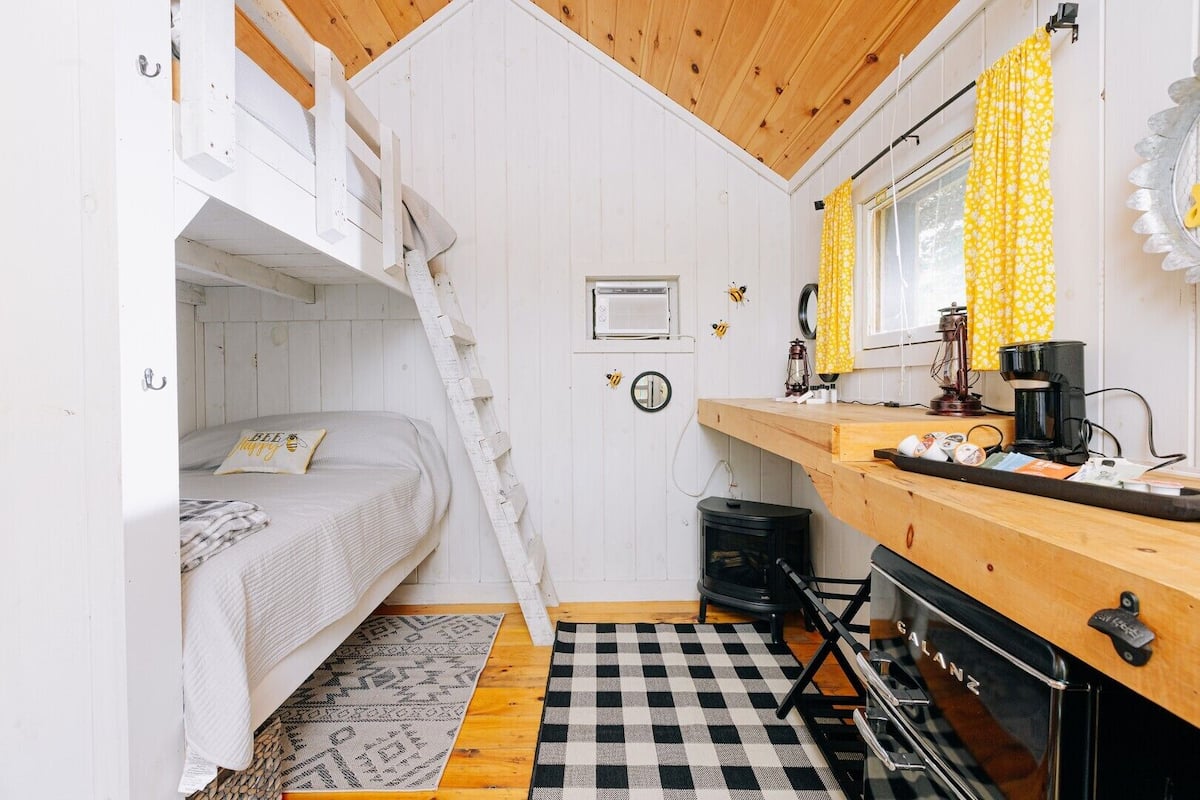 A compact room with a bunk bed, a small kitchen area with a stove, and a checkered floor.