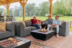 A covered outdoor seating area with a fire feature, a grill, and a patterned rug. - Battenkill Glamping Resort (Cambridge)