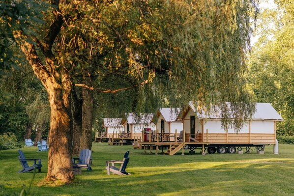 A row of wooden cabins with a deck and a covered area, surrounded by trees and grass. - Battenkill Glamping Resort (Cambridge)