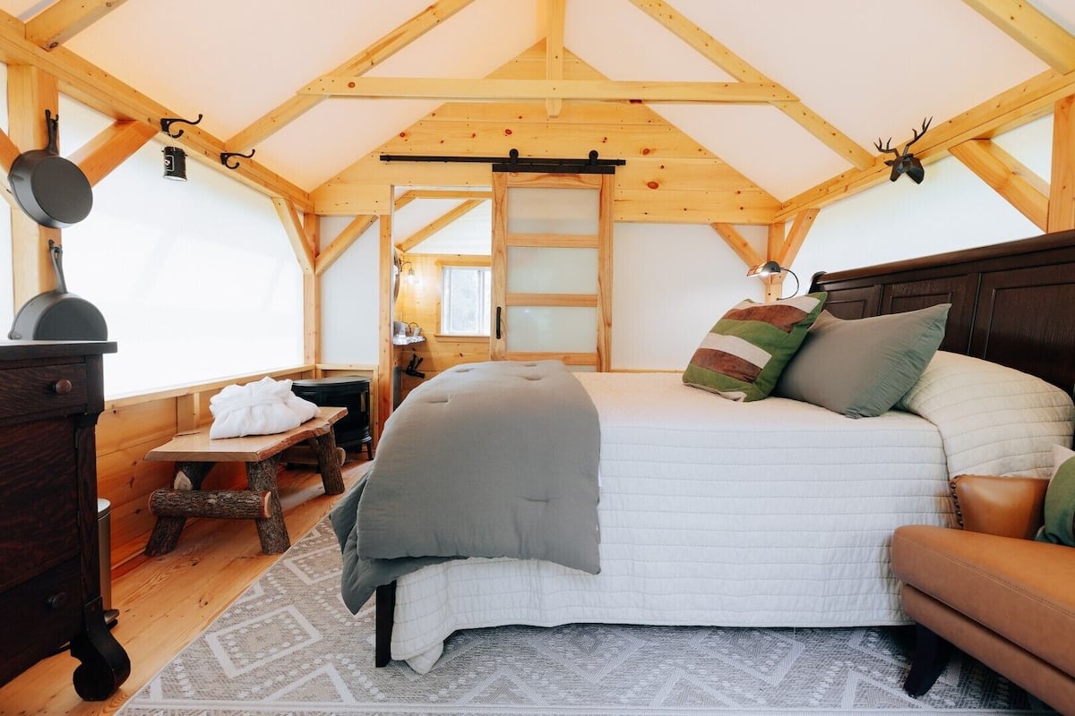 A cozy bedroom with a bed, a dresser, a table, and a fireplace.