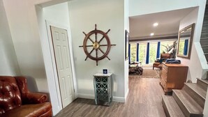 A spacious living area with a leather sofa, a wooden floor, a ship's wheel decoration, and a staircase leading to another room. - 3 Story Rainbow Riverfront House With Panoramic Views!  (Dunnellon)