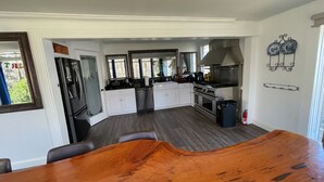 A modern kitchen with white cabinets, a stainless steel stove, and a large wooden dining table. - 3 Story Rainbow Riverfront House With Panoramic Views!  (Dunnellon)