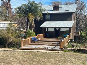A wooden house with a deck, a covered porch, and a flag. - 3 Story Rainbow Riverfront House With Panoramic Views!  (Dunnellon)