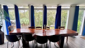 A conference room with a large wooden table and six chairs, large windows with blue curtains, and a view of greenery outside. - 3 Story Rainbow Riverfront House With Panoramic Views!  (Dunnellon)
