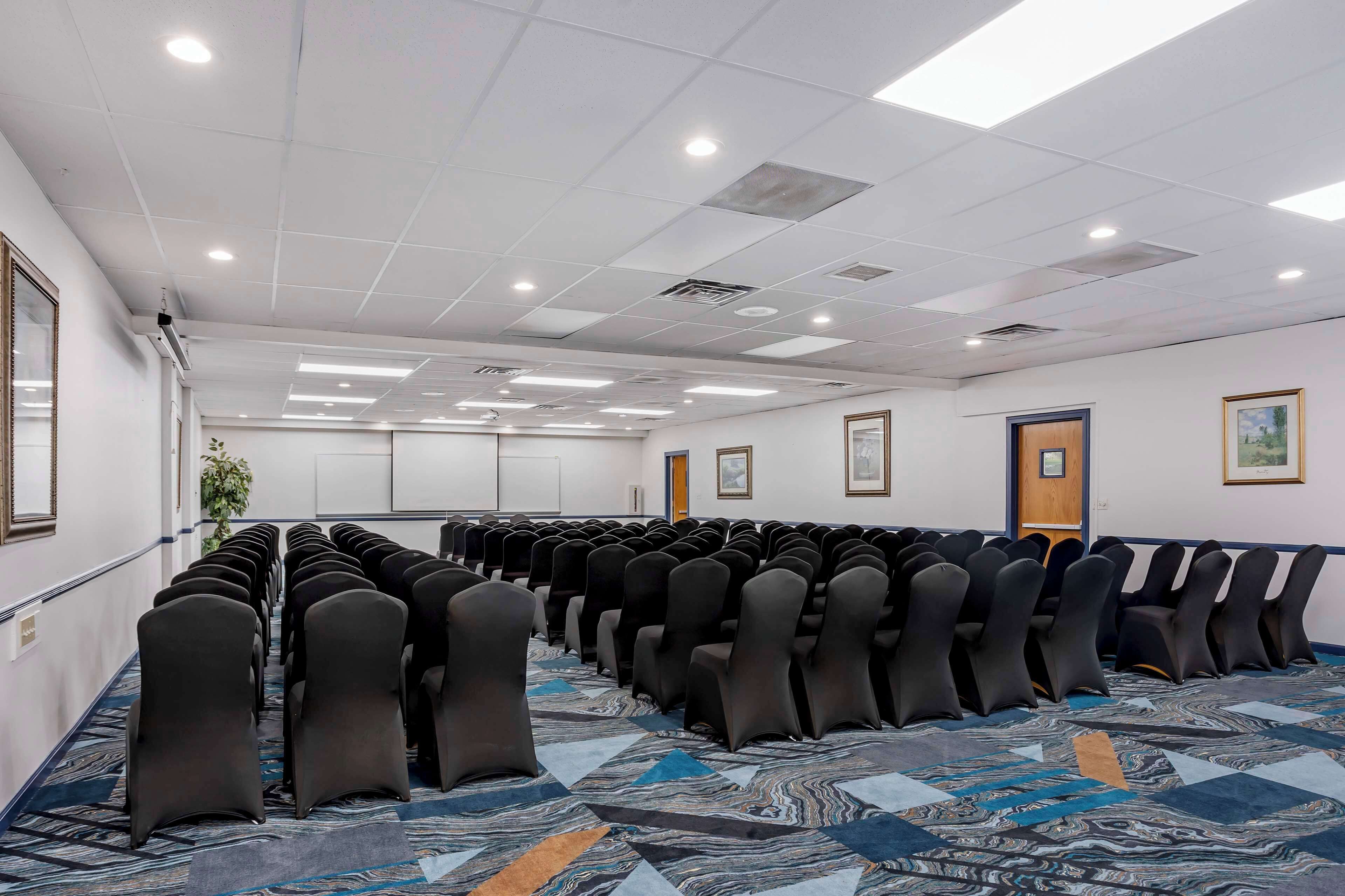 Une salle de conférence avec des rangées de chaises, une moquette à motifs et un plafond blanc doté d’un éclairage encastré.