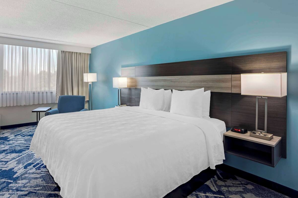 A hotel room with a large bed, two bedside lamps, a nightstand, and a chair.