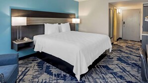 A hotel room with a large bed, a nightstand with a lamp, a chair, and a door leading to another room. - Best Western New Brunswick - East Brunswick (East Brunswick)