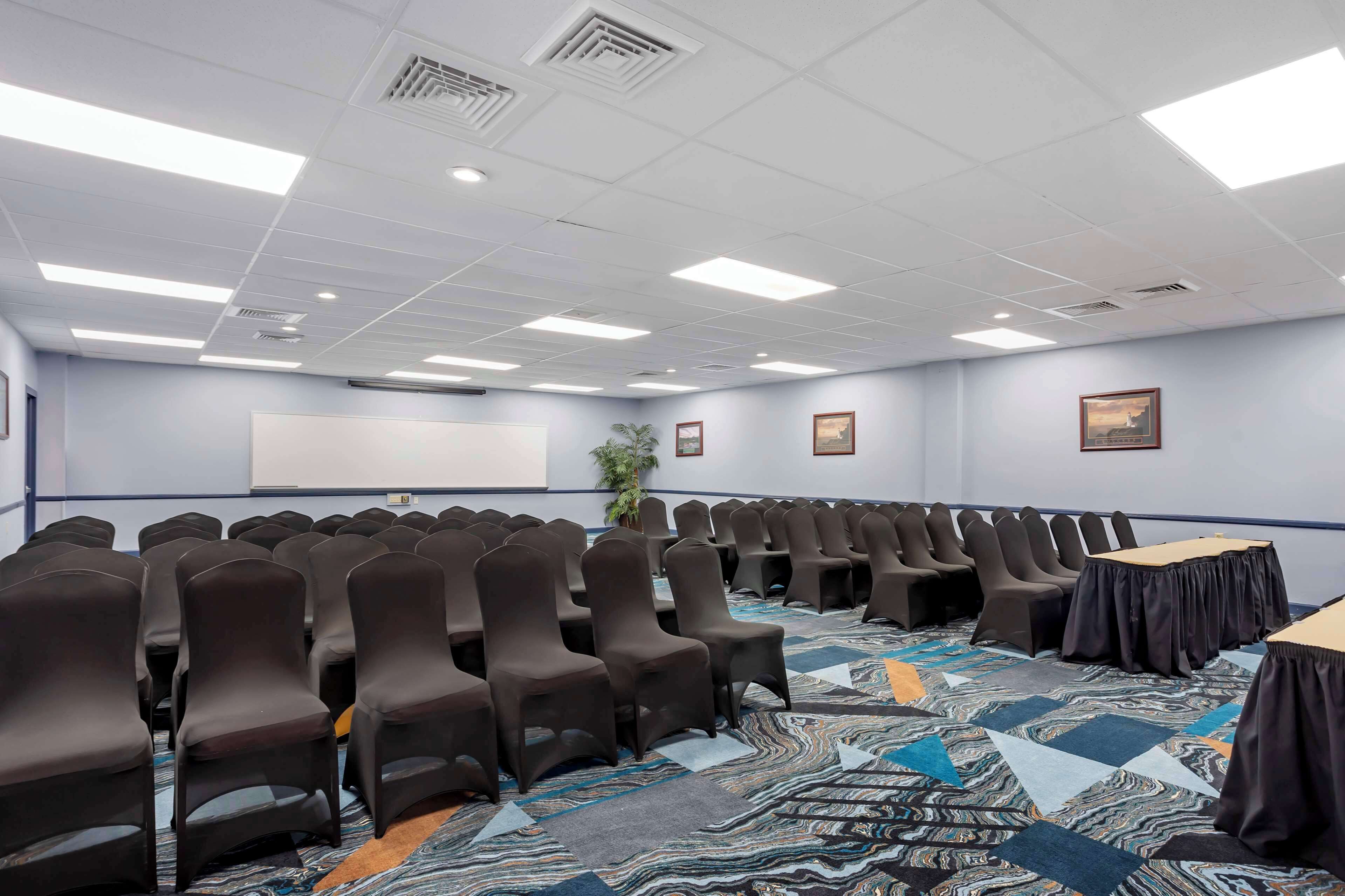 A conference room with rows of chairs, a large whiteboard, and a patterned carpet.