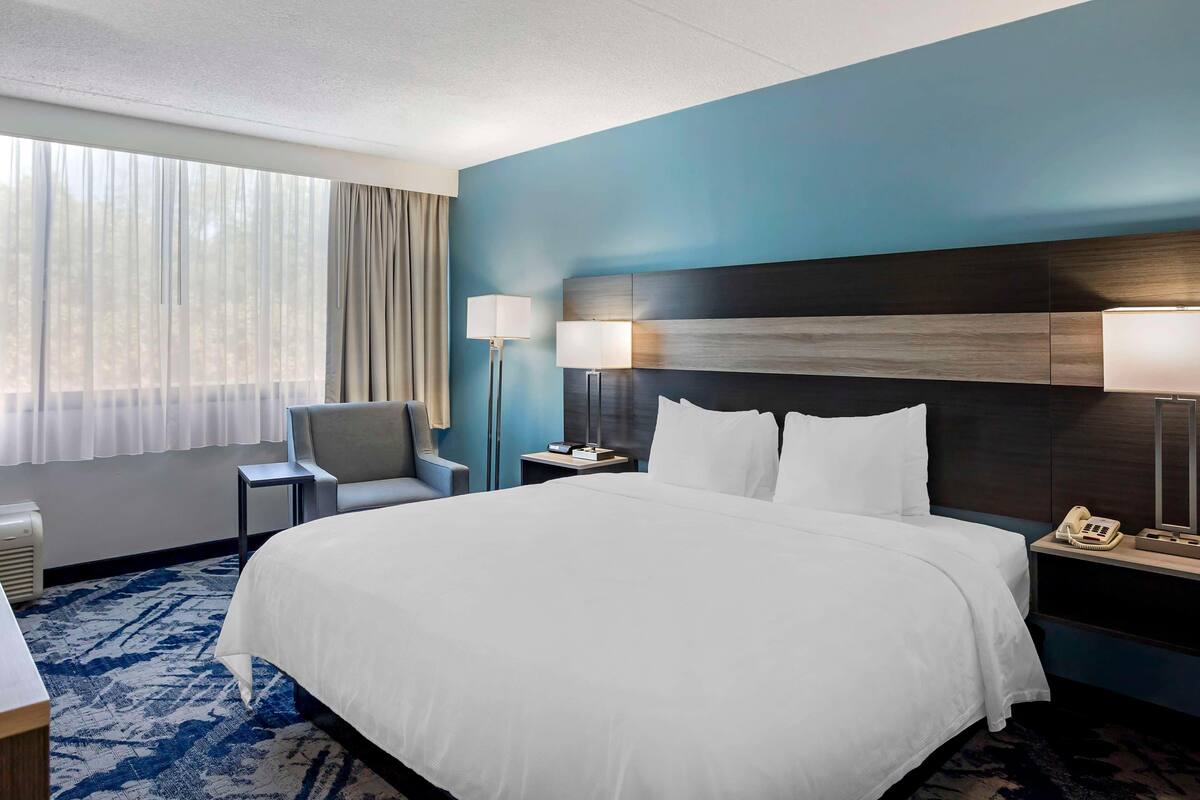 A hotel room with a large bed, a chair, a desk, a lamp, and a telephone.