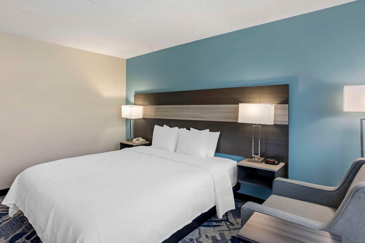 A hotel room with a large bed, two bedside lamps, a nightstand, and a chair.