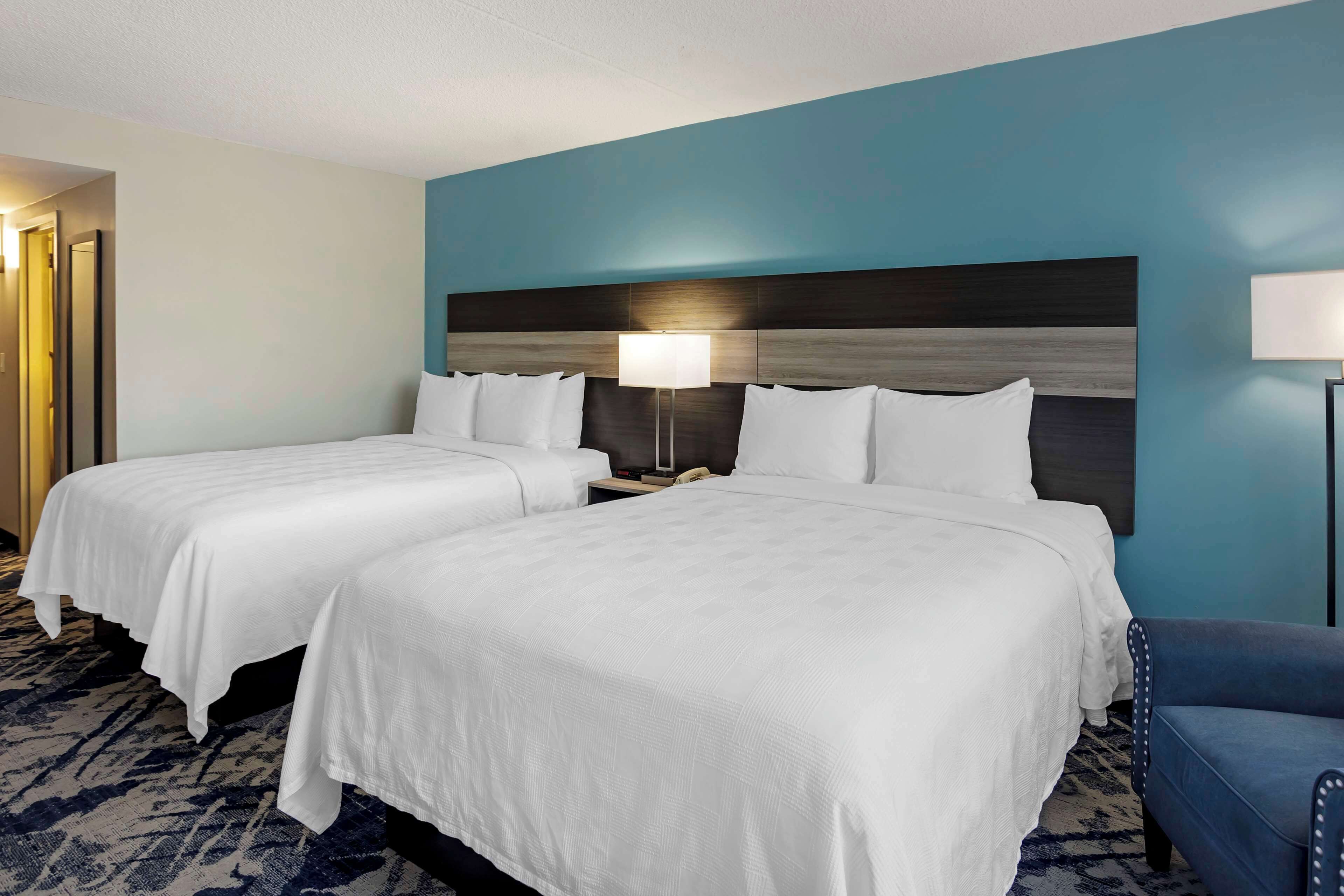 Ein Hotelzimmer mit zwei Betten, einer blauen Akzentwand und einem blauen Sessel.