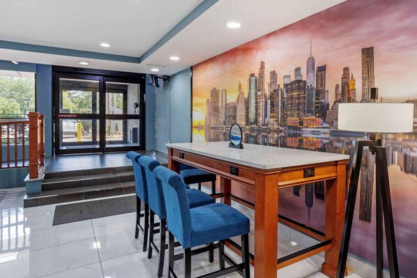 Vestíbulo de hotel con un mural de la ciudad, una recepción y taburetes azules.