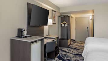 A hotel room with a bed, a desk with a chair, a television, a coffee maker, and a wardrobe.