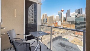 A balcony with a table and chairs, offering a city view with tall buildings and a tower. - City View 1BR Downtown Calgary (Calgary)