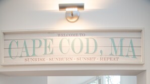 A dining area with a wooden table and chairs, a mirror, and a sign above welcoming visitors to Cape Cod, MA.