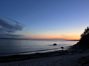 Una playa con agua tranquila, un litoral rocoso y un cielo despejado.