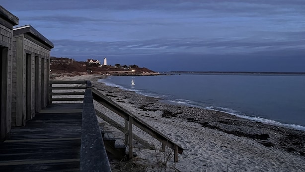 A wooden boardwalk leading to a beach with a lighthouse in the distance.