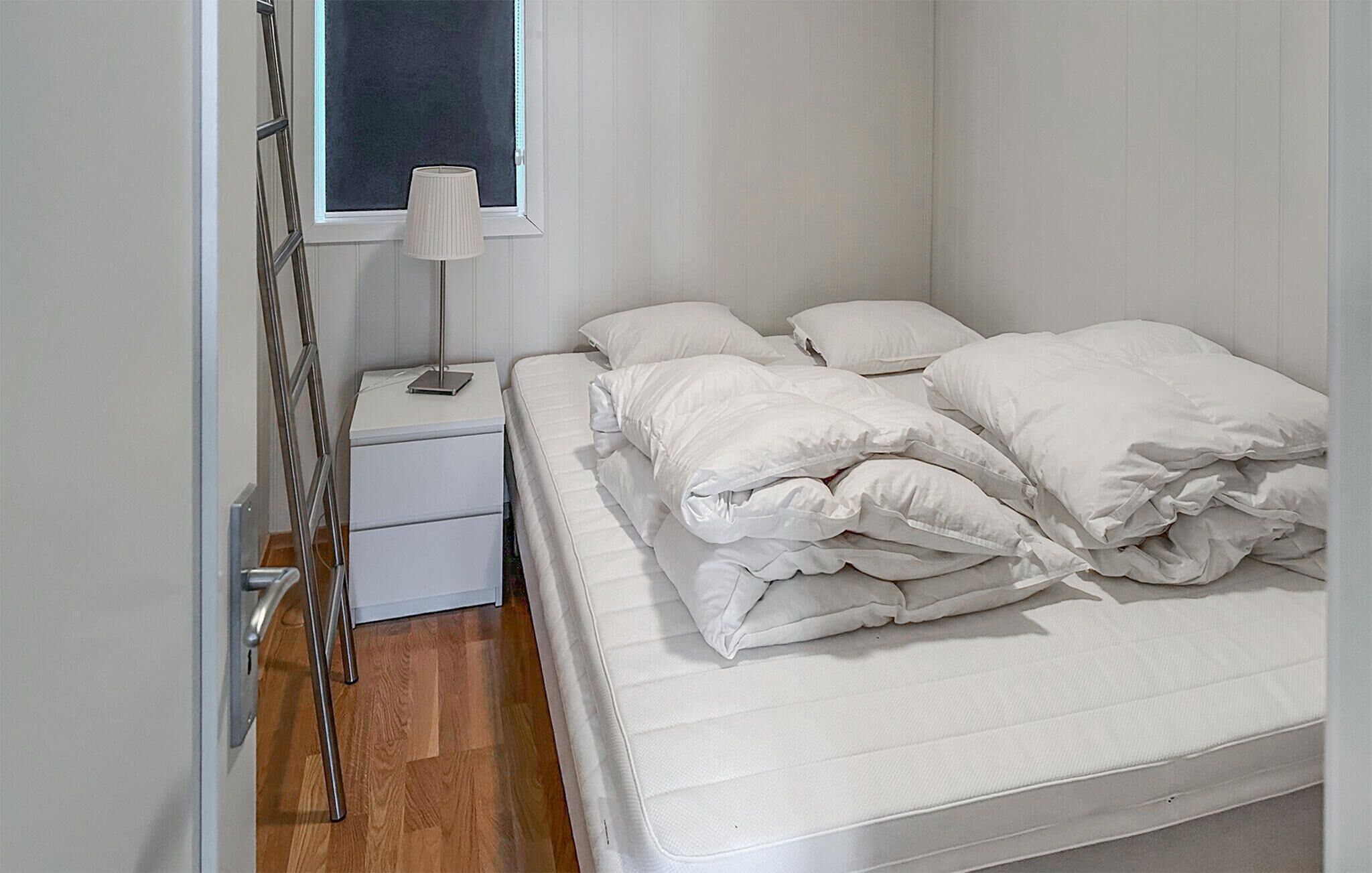 A small, neatly made bed with white bedding in a room with white walls and a window.