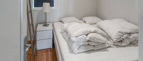 A small, neatly made bed with white bedding in a room with white walls and a window.