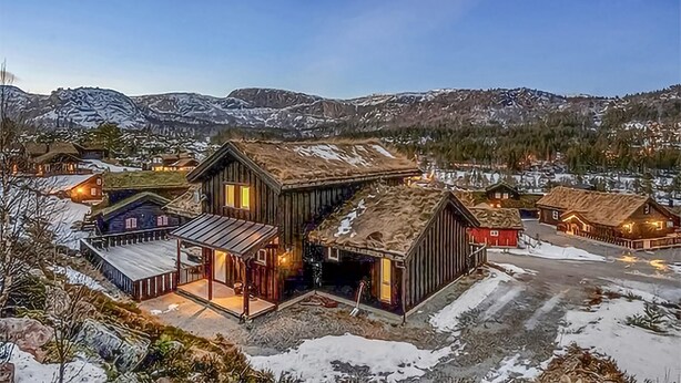 A rustic cabin with a large porch and a garage, surrounded by snow-covered mountains and other wooden buildings. - Nice home in Rysstad with WiFi (Rysstad)