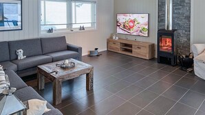 A modern living room with a grey sofa, a wooden coffee table, a TV, a fireplace, and a stone wall. - Nice home in Rysstad with WiFi (Rysstad)