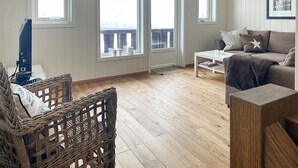 A living room with a wooden floor, a wicker chair, a sofa, and a coffee table. There are windows with a view of the outside. - Nice home in Rysstad with WiFi (Rysstad)