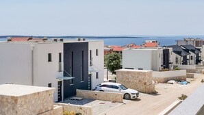 Un quartier résidentiel moderne avec une voiture blanche garée dans une allée, des murs en pierre et une vue sur la mer.