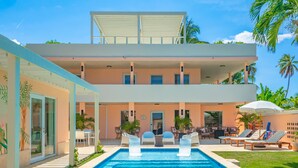 Un edificio de dos pisos con piscina, mobiliario exterior y palmeras.
