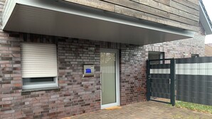 Ein Backsteinhaus mit einem verschlossenen Eingang, einem Briefkasten und einem Fenster mit Rollläden.