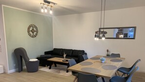 Ein modernes Wohnzimmer mit einer schwarzen Couch, einem Holztisch und einem Esstisch mit Stühlen.
