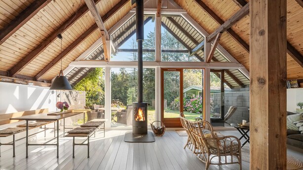 Amplia habitación en ático con techos altos de madera, chimenea y vistas al jardín.