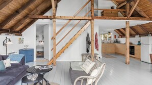 Un loft espacioso con vigas de madera a la vista, una cocina con armarios de madera, un comedor con mesa y sillas, y una sala de estar con sofá y una mesita redonda.