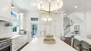 A spacious kitchen with white cabinetry, a central island, and a modern chandelier. - Park Place 251 LAU (Port Aransas)