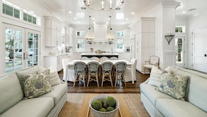 A spacious kitchen with white cabinetry, a central island with chairs, and a chandelier. - Park Place 251 LAU (Port Aransas)