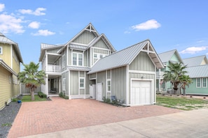 A two-story house with a front porch, a garage, and a brick driveway. - In II Deep 123 FI (Port Aransas)