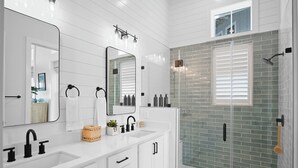 Un baño moderno con un tocador blanco, dos espejos, cabina de ducha de vidrio y una ventana pequeña.