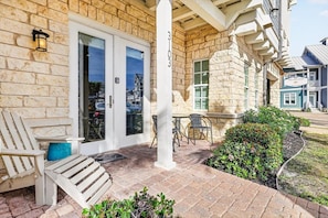 A stone building with a porch, outdoor seating, and a visible door. - Beach Haven TC 3103 (Port Aransas)