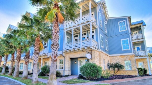 A multi-story hotel with a blue exterior, a balcony on the second floor, and palm trees in the foreground. - Beach Haven TC 3103 (Port Aransas)
