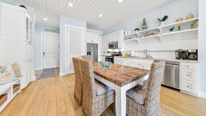 A modern kitchen with white cabinetry, a central island, and a dining area with wicker chairs. - Beach Haven TC 3103 (Port Aransas)