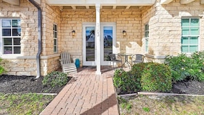 A stone building with a covered patio, two doors, and outdoor seating. - Beach Haven TC 3103 (Port Aransas)