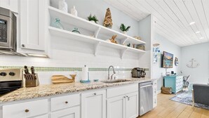 A modern kitchen with white cabinetry, a granite countertop, and a built-in oven. - Beach Haven TC 3103 (Port Aransas)