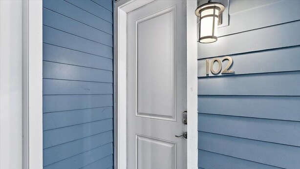 A white door with a keypad lock, a number '102' on the wall, and a wall-mounted light fixture. - Palm Tree Retreat TC 3102 (Port Aransas)