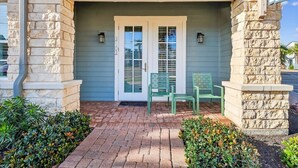 A house with a stone facade, a front door with glass panels, and two green chairs outside. - Palm Tree Retreat TC 3102 (Port Aransas)