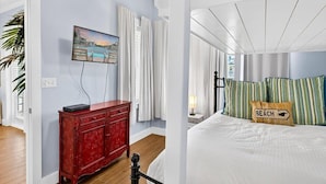 A hotel room with a bed, a red cabinet, a painting, and a view of the outdoors. - Palm Tree Retreat TC 3102 (Port Aransas)