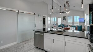 A modern kitchen with a dishwasher, a large island, and a dining area with a TV. - Bajo El Sol 124 SEV (Port Aransas)