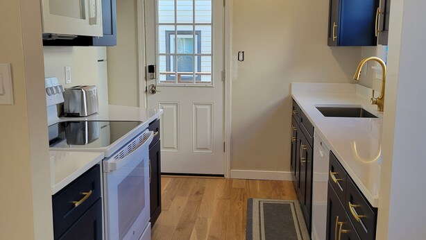 A compact kitchen with white appliances, dark cabinets, and a wooden floor.