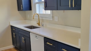 A modern kitchen with dark cabinetry, white countertops, and a gold faucet.