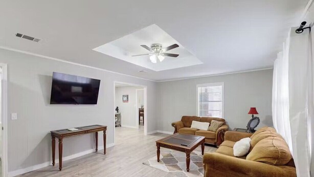 Una sala de estar con ventilador de techo, televisor de pantalla plana, sofá marrón y una mesa de centro.